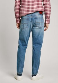 Blue denim jeans with a slightly faded finish, straight cut, and rear pockets featuring a diamond shape. Paired with white sneakers.