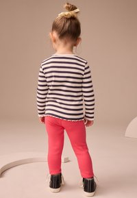 Striped long-sleeve top in navy and white, paired with bright pink leggings. The top features a scalloped hem, and black shoes complete the look.