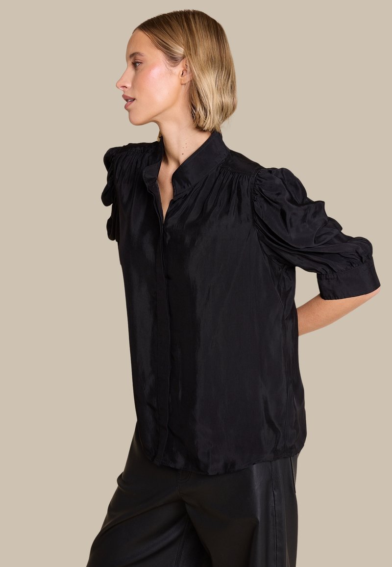 Svart satengbluse med korte puffede ærmer, mandarin-krave og en lidt løs pasform. Glat tekstur, minimalistisk design.