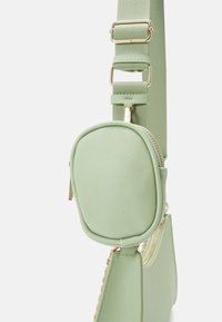 Sac bandoulière texturé vert clair avec deux compartiments zippés et une bandoulière large et réglable avec quincaillerie dorée.