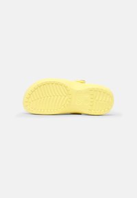 Semelle jaune de Crocs avec un motif de bande de roulement texturé visible sur un fond blanc uni.