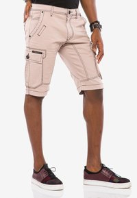 Helle beige Cargo-Shorts mit Steppdetails und Seitentaschen, im lässigen Schnitt mit umgeschlagenen Säumen, kombiniert mit dunklen, gemusterten Sneakern.