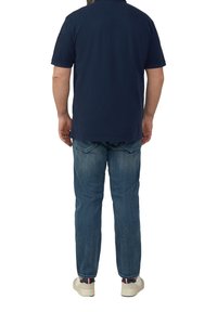 Granatowa koszulka polo, krótki rękaw, materiał bawełniany; w połączeniu z jasnoniebieskimi dżinsami, widok z tyłu; casualowe białe sneakersy z akcentującymi kolorami.