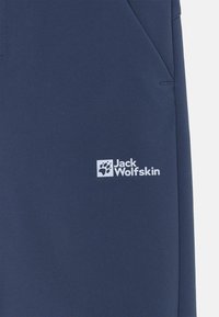 Navy blue outdoor pants made of soft, technical fabric. Features a logo in white and side pockets with angled openings.