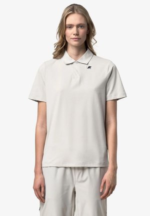 Donna che indossa una polo a maniche corte grigio chiaro con colletto e piccolo logo sul petto sinistro, abbinata a pantaloni grigio chiaro coordinati.