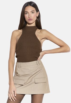 Top marrón de canalé con cuello halter combinado con una minifalda beige que tiene dos bolsillos delanteros y trabillas para cinturón. Texturas suaves y diseño ajustado.