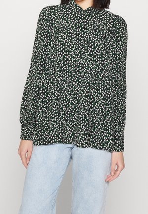 Zwarte bloes met witte en groene bloemenpatronen, een kraag met knopen en een geplooid ontwerp. Lange mouwen, lichtgewicht stof en een losse pasvorm.