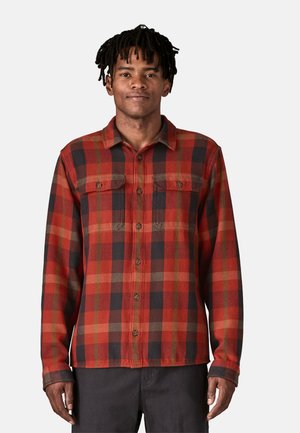 Camicia in flanella a quadri rossi e neri con maniche lunghe, chiusura con bottoni sul davanti, due tasche sul petto e colletto. Tessuto textured con un aspetto caldo.
