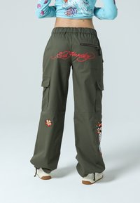 Olivgröna cargo-byxor med avslappnad passform, prydda med broderade blommönster och en logotyp i röd. Inkluderar sidfickor och en ficka med dragkedja.