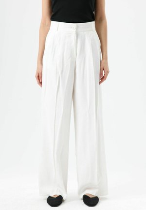 Witte, hooggetailleerde, broek met wijd uitlopende pijpen, voorplooien en een enkele knoopsluiting, gemaakt van lichtgewicht stof. Zwarte platte schoenen gedragen.