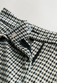 Vävt tyg med ett hundtandsmönster i svarta, vita och bruna nyanser. Inkluderar knappstängning och kontrasterande svart kant.