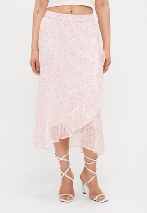 Jupe midi fleurie rose pâle avec un ourlet à volants portée avec des sandales blanches à talons hauts et à lanières et un top court blanc.