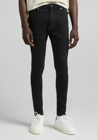 Pantalones vaqueros ajustados negros hechos de mezclilla con una textura suave, que cuentan con dos bolsillos delanteros, cierre de botón y ligera elasticidad para mayor comodidad.
