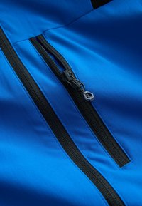 Tissu bleu avec deux fermetures éclair noires, dont une partiellement ouverte avec un tirette hexagonal attaché à une boucle de corde.