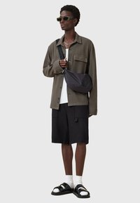 Dark green button-up shirt over a white T-shirt, paired with black cargo shorts and black sandals. Includes a crossbody bag.