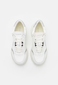 Zapatillas deportivas de cuero blanco con acentos de malla, suela de goma texturizada y detalles contrastantes en negro y plata. Cordones y logotipo en la lengüeta.