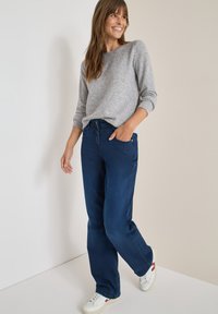 Mörkblå jeans med avslappnad passform och upphöjda sömmar, i kombination med en ljusgrå strukturerad tröja och vita sneakers. Snygg, avslappnad stil.