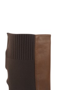 Bruine leren boots met donker gebreid stof en een geribbelde bovenkant, en een glad leren paneel, die texturen combineren voor contrast en comfort.