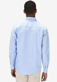 Vaaleansininen pitkähihaisessa paidassa on napillinen kaulus, takakappale ja kaksi napilla varustettua hihansuuta. Valmistettu sileästä kudotusta kankaasta.