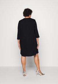 Svart knälång klänning med trekvartsärmar och rund halsringning. Tillsammans med silverfärgade högklackade skor. Enkel, ren design.