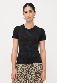 Zwart shirt met korte mouwen met een geribbelde textuur en een wit gestippeld patroon. Gecombineerd met broek met luipaardprint.