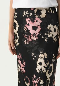 Jupe midi florale noire avec des fleurs roses et crème. Tissu lisse, design ajusté, longueur mi-mollet, avec un subtil éclat.