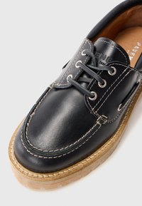 Schwarzer Lederschuh mit runder Zehenpartie und gesticktem Design, ausgestattet mit silbernen Ösen und einer hellbraunen Gummisohle. Glatte Textur und klassischer Stil.
