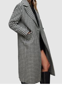 Mantel mit Hahnentritt-Muster in Schwarz und Weiß, mit Kragen, langen Ärmeln, vorderen Taschen und knielangem Schnitt.