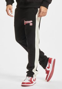 Juodi sportiniai džinsai su baltais šoninėmis juostelėmis, su raudonu "Rocawear 99" logotipu. Derinami su raudonais ir baltais sportiniais bateliais. Minkšta medžiaga, laisvas fasonas.