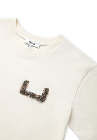 Crème katoenen t-shirt met een textuur en kralen 'U' ontwerp in grijs en oranje tinten op de borst. Klassieke ronde hals, korte mouwen.