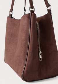 Καφέ σουέντ τσάντα χειρός με ασημένια φερμουάρ και διπλούς ιμάντες ώμου, πάνω σε απλό ανοιχτόχρωμο φόντο.