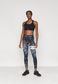 Black sports bra with cross-back design; colorful patterned leggings featuring dark tones and abstract accents; black athletic shoes.