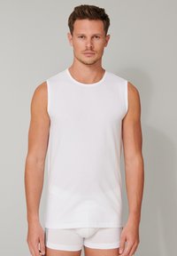 Vit ärmlös tanktopp av mjukt tyg, med rund halsringning och en enkel design, bärs över vita trosor.