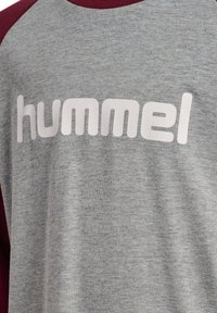 Grå crewneck t-shirt med burgundy ærmer, der har et fremtrædende hvidt "hummel" logo på forsiden, lavet af blødt stof.