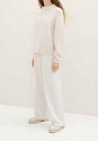 Pull en tricot rose clair avec un col montant et des poignets côtelés, associé à un pantalon large blanc et des chaussures à plateforme crème.