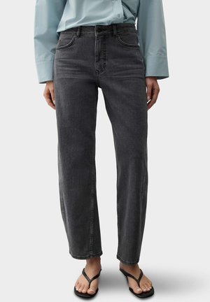 Person trägt eine hochtaillierte, schwarze, gerade Jeans mit einem hellblauen Langarmhemd und schwarzen offenen Sandaletten mit Absatz.
