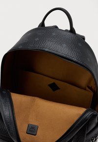 Mochila de cuero negro texturizado abierta que revela un interior de ante marrón con un bolsillo deslizante y un parche de logo de la marca negro en el interior.