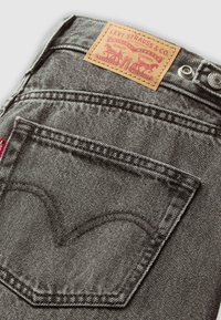 Tuvumā izskatāmi pelēkie Levi's džinsi ar priekšējo kabatu, kurā redzams raksturīgais sarkanais tab un ādas zīmols virs jostas.