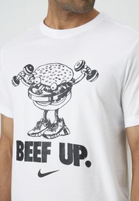 White cotton t-shirt featuring a graphic of a cartoon hamburger lifting dumbbells, with text "BEEF UP" in bold black, next to a Nike logo.