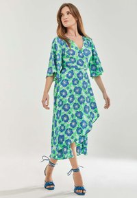Floral wrap dress in green and blue with a V-neck, flutter sleeves, and an asymmetric hem. Paired with blue strappy sandals.