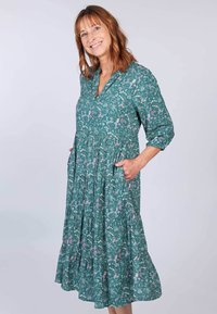 Tee-farbene Blumenkleid mit 3/4-Ärmeln, knöpfbarem Ausschnitt und zwei seitlichen Taschen. Mit gerafften Stufen und einer schwingenden, knielangen Silhouette.