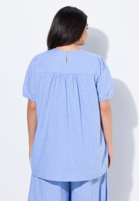 Blusa di cotone azzurro chiaro con maniche corte a sbuffo, dettaglio a chiave sulla schiena e tessuto arricciato sul giromanica per una vestibilità comoda.