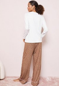 Bílý dlouhý rukáv top a hnědé kalhoty s puntíky vyrobené z hladkého materiálu s volným střihem. Kalhoty mají světlou šňůrku na manžetách.