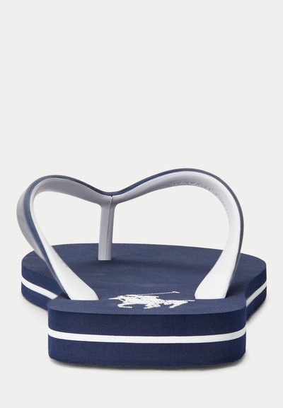 Tums zils pludmales čības ar baltu dubulto svītru uz zolītes un baltu polo spēlētāja siluetu uz pēdas daļas, skatīts no aizmugures.