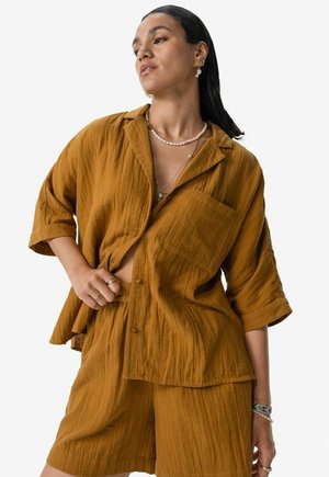 Chemise légère de couleur bronze, texturée, avec des manches courtes et une poche, assortie à un short.