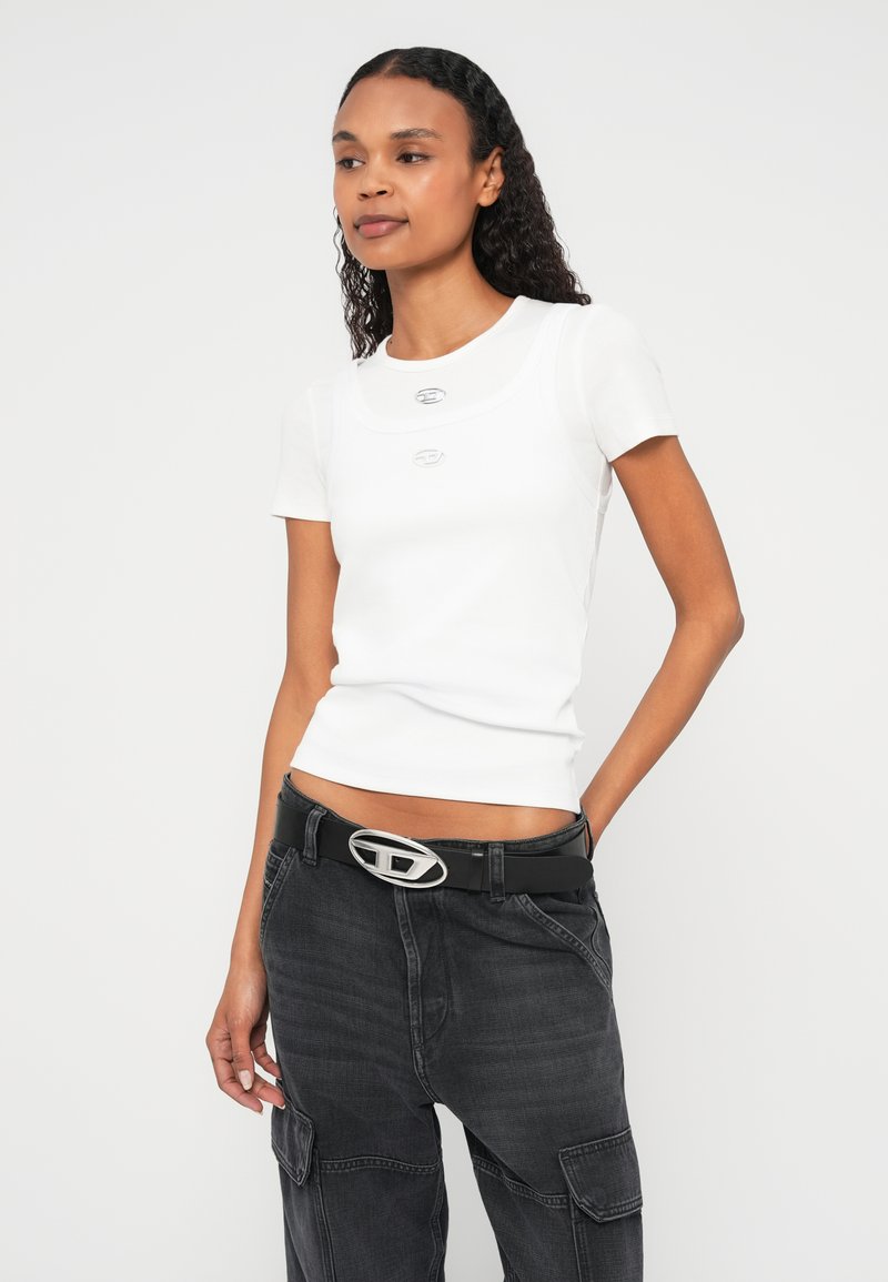 Hvid tætsiddende t-shirt med korte ærmer og dekorative sølvknapper, kombineret med højtaljede sorte cargobukser med bredt bælte.