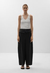 Débardeur blanc côtelé avec un col en V, associé à un pantalon noir ample avec une taille repliée et des sandales plates.