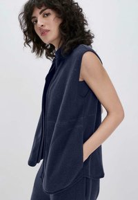Marineblaue Fleece-Weste mit ärmellosem Design, Reißverschluss und Seitentaschen; verfügt über einen strukturierten Stoff und einen lockeren Schnitt.