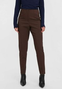 Braune, taillierte Hose mit hoher Taille, glatter Textur und ordentlichen Falten, kombiniert mit spitzen schwarzen Stiefeletten.