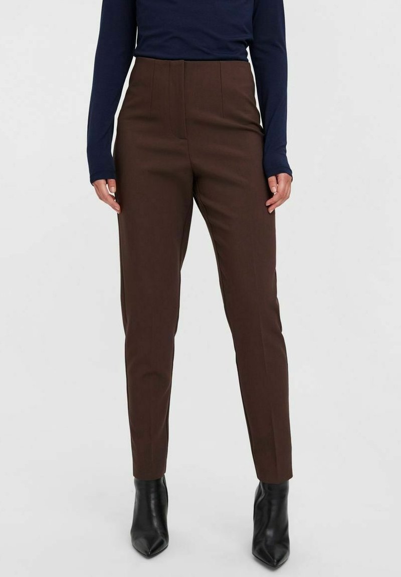 Braune, taillierte Hose mit hoher Taille, glatter Textur und ordentlichen Falten, kombiniert mit spitzen schwarzen Stiefeletten.